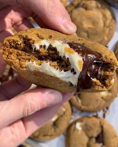 a person holding a chocolate chip cookie with white frosting and cookies in the background