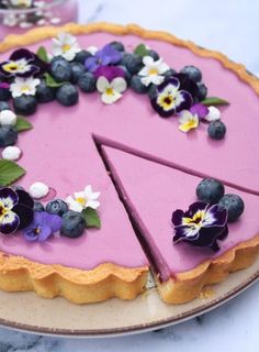 a pink pie with blueberries and pansies on the top is ready to be eaten