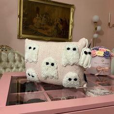 a white teddy bear pillow sitting on top of a pink table next to a painting