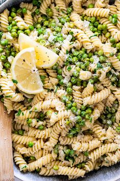 a bowl filled with pasta, peas and lemon wedges