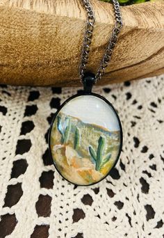 a glass caballon necklace with a desert scene in the background on a black chain