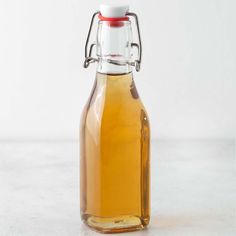 a glass bottle filled with liquid sitting on top of a white counter next to a red lid