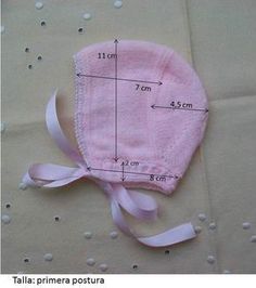 a baby's pink hat with a bow on the side and measurements for it