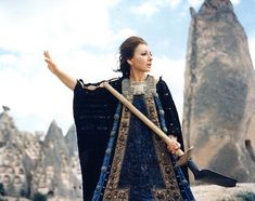 a woman dressed in medieval clothing holding a shovel and pointing to the sky with her right hand