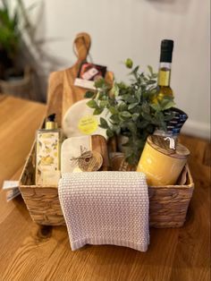 a wooden table topped with a basket filled with food and wine bottles next to a potted plant