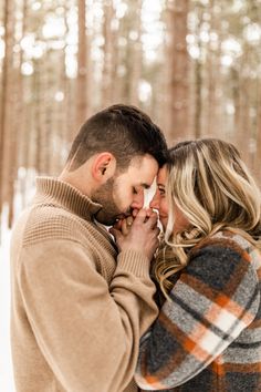 a man and woman standing next to each other in front of trees with snow on the ground