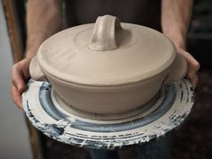 a person holding a clay pot on top of a white and blue plate in their hands