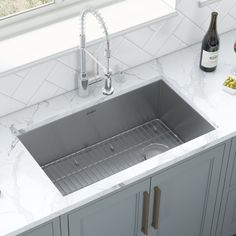 a stainless steel kitchen sink and countertop with wine bottle on the window sill