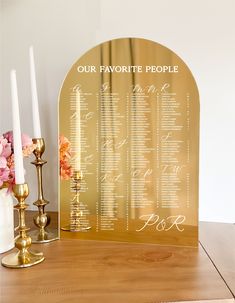 a gold wedding seating chart on a table with candles and flowers in front of it