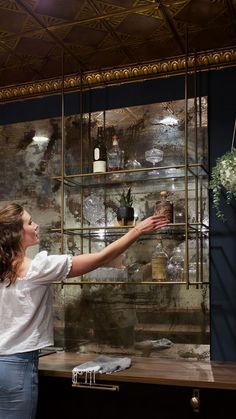 a woman is reaching out for something in a glass case with flowers on the shelves