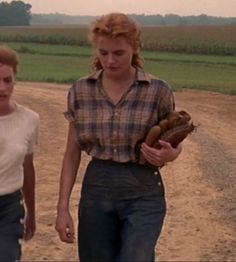 two women walking down a dirt road holding baseball mitts in their hands and looking at the camera