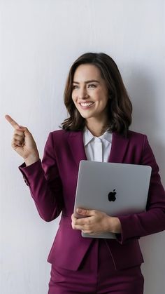 a woman in a purple suit pointing at an apple laptop computer with her finger up