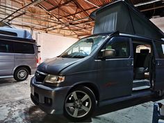 a silver van parked in a garage next to another van with its door open and the roof opened