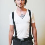 a man with suspenders and a white t - shirt is standing in front of a wall