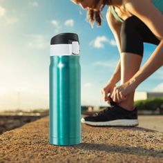 a woman tying her shoe while standing on the side of a road next to a water bottle