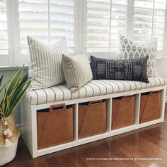 a white bench with some baskets on top of it next to a plant and window