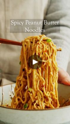 a person holding chopsticks over noodles in a bowl with the caption spicy peanut butter noodles