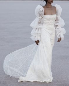 a woman in a white dress walking on the beach with her veil blowing up over her head