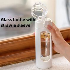 a person is holding a glass bottle with straw and sleeve on the window sill