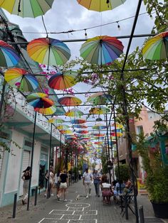 many colorful umbrellas are hanging from the ceiling over a street lined with people walking down it