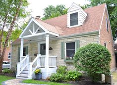 a small brick house with white trim and green shutters on the front porch is shown