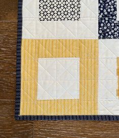 a close up of a quilt on a wooden floor with white and yellow squares in the center