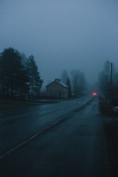 a foggy street with a red car on the road and houses in the background