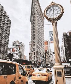 a clock on a pole in the middle of a busy street with taxis and taxi cabs