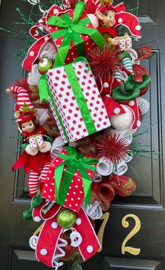 a christmas wreath on the front door with presents tied to it and elfs around it