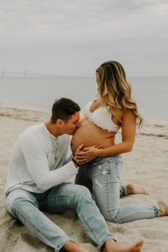 a pregnant couple sitting on the beach with their belly wrapped around each other and kissing