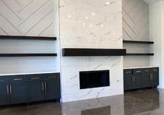 an empty room with white walls and black cabinets in the center, along with marble fireplace mantels