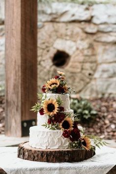 a three tiered cake with sunflowers and red flowers on the top layer