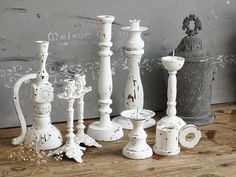 several white candlesticks are lined up on a table next to a gray vase