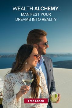 a man and woman standing next to each other holding wine glasses in front of the ocean