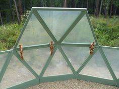 a green metal and glass structure in the middle of a forest