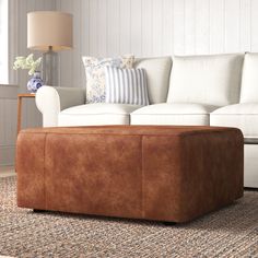 a living room with a couch, ottoman and lamp on the side table in front of it