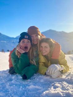 three women are laying in the snow and posing for a photo with their arms around each other