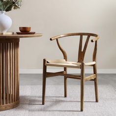 a wooden chair next to a table with a vase on it and a white flower in the background