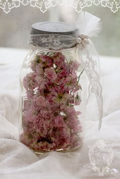 a jar filled with pink flowers sitting on top of a white bed sheet next to a lace doily