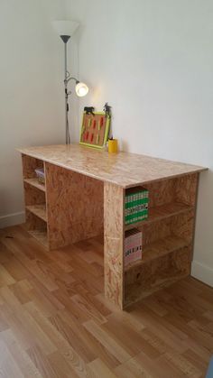 a desk made out of plywood is sitting on the floor in front of a lamp