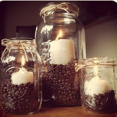 three mason jars filled with coffee beans and lit candles on top of a wooden table