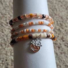 Handmade Halloween Stretch Bracelets. Four Bracelets Total. Colors Are White, Cream, Brown, Orange And Silver With A Pumpkin And Ghost Charm. Halloween Inspired Bracelets, Halloween Stretch Bracelets, Beaded Bracelets Fall, Handmade Orange Novelty Bracelets, Heishi Bracelet Ideas Fall, Autumn Bracelet Ideas, Halloween Beaded Bracelet, Fall Beaded Jewelry, Fall Beaded Bracelets