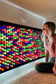 a woman sitting on the floor in front of a wall with colorful lights behind her