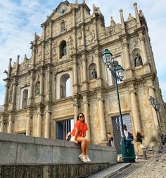 a woman in an orange shirt is sitting on the steps next to a large building