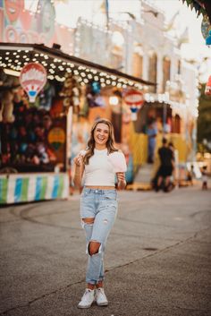 a woman standing on the street in front of an amusement park with lights and carnival rides