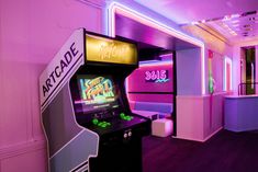 an arcade machine with neon lights in a pink and purple room that has couches