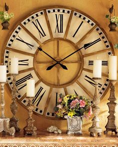 a large clock with roman numerals on the face and candles in front of it