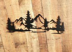 a wooden wall with some cut out trees and mountains on it in front of a fence