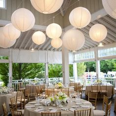 a room filled with lots of tables covered in white paper lanterns and round tablecloths