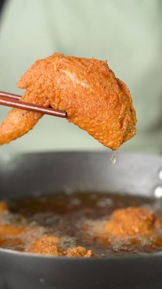 fried chicken being lifted from a pan with chopsticks